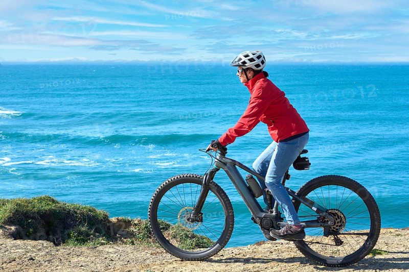 Active senior woman riding her electric mountain bike on the rocky cliffs of Peniche at the western atlantic coast of Portugal