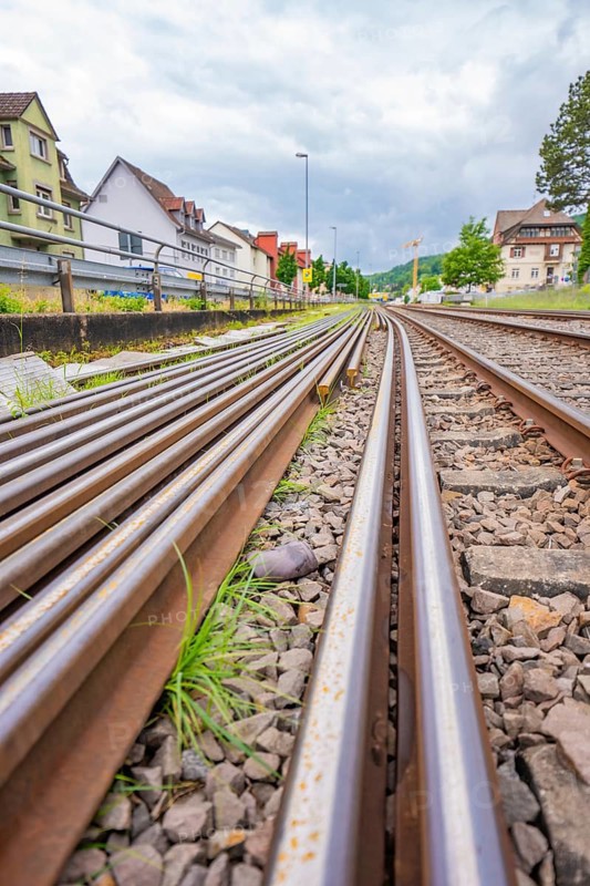 Railway tracks with gravel flanked by buildings and vegetation under cloudy skies, Leonhard Weiß electrification station conversion, Waldshut. germany