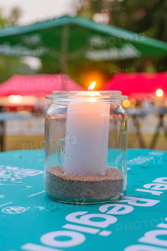 Burning candle in a glass, outside on a table with evening lighting with colorful shades in the background, Calwer Klostersommer Festival, Hirsau Abbey, Calw, Germany