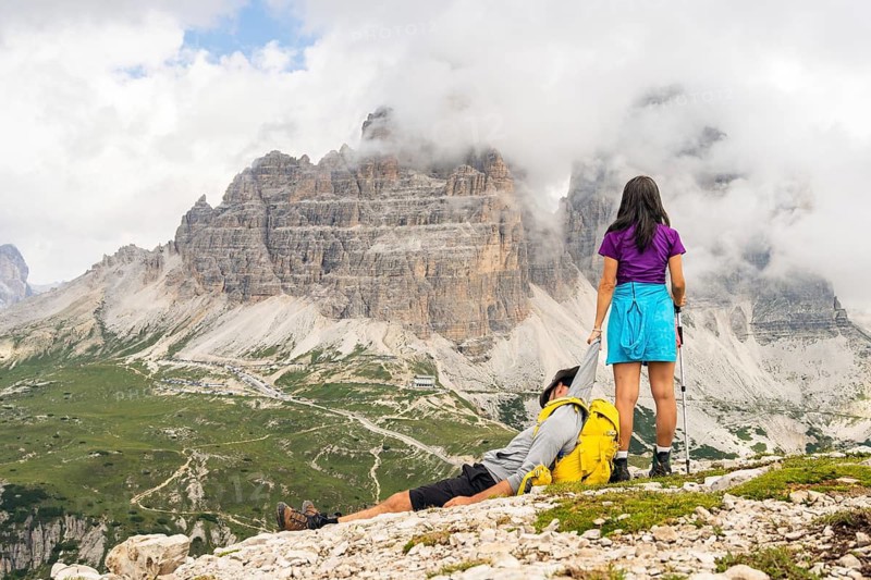 Woman helping exhausted hiking partner boyfriend dragging in Dolomites mountains. Teamwork leadership support trust resilience and shared success moments. Funny meme mock up moments. Italy. Dolomites