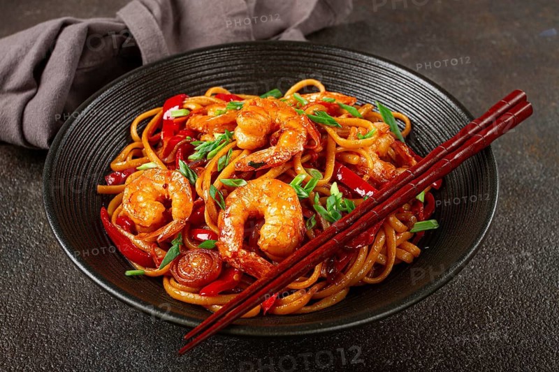 Udon stir-fry shrimp noodles with red bell pepper and green onion, served in a black bowl, with chopsticks, dark background