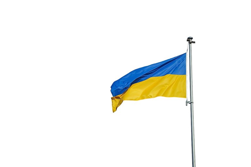 The Ukrainian national flag with blue and yellow horizontal bands is shown isolated on a white background. The fabric appears slightly curved, revealing the simple two color design and clear geometric layout. The clean isolation emphasizes the symbol, its colors, and its national identity without any surrounding environment