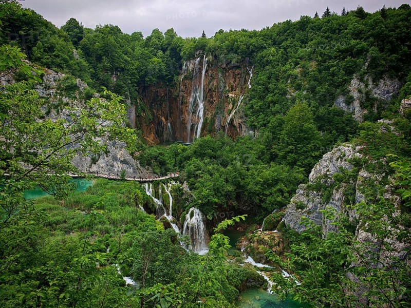 Scenery with waterfalls and bridge on which tourists hike in a wooded area, Plitvice Lakes National Park, Croatia