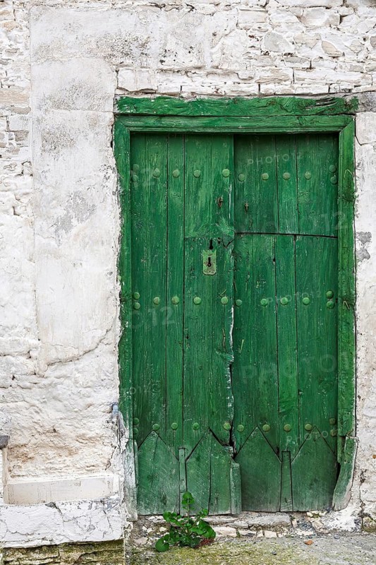 An old green wooden door in a weathered stone wall, looks rustic and historic, Cyprus