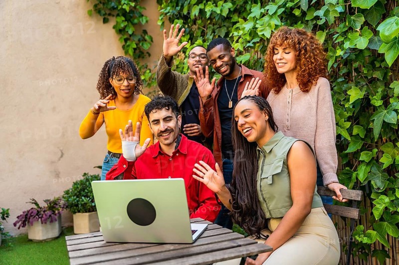Diverse young people enjoying a virtual group therapy session or online support meeting, engaging with friends and communicating remotely through a laptop on a wooden outdoor table