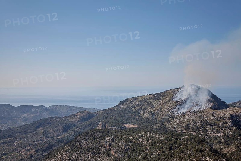 Smoke rises from a forest fire in a mountainous landscape, the sky is clear and blue, Majorca, Balearic Islands, Spain