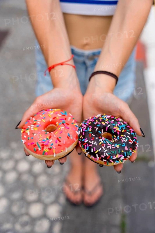 Woman's hands presenting two delicious frosted donuts with colorful sprinkles, offering a sweet indulgence and choice for a happy lifestyle