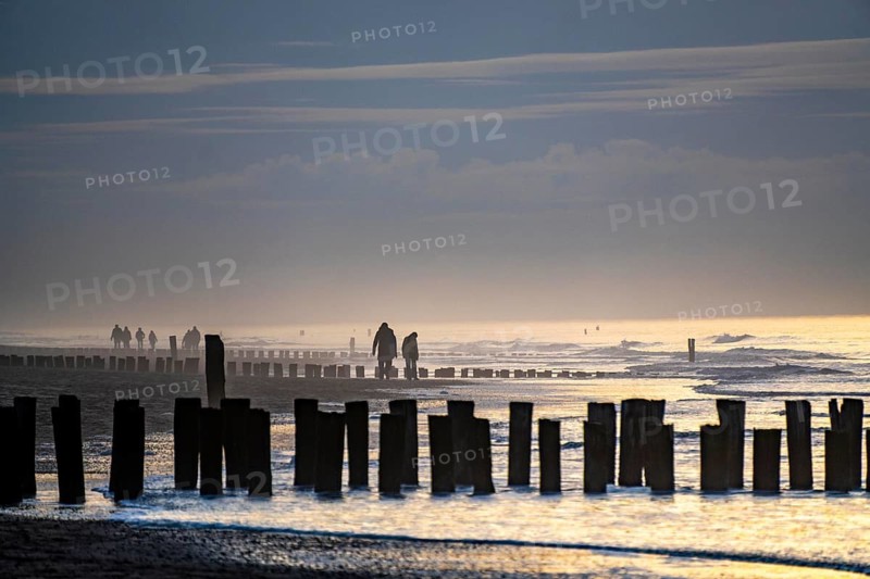 Winter on the North Sea, sunset at sea, beach walkers, coastal protection, through wooden posts, paalhoofden, on the beach, breakwater, the piles rammed into the sandy soil in double rows slow down the waves and ocean currents and thus slow down the flow rate of seawater, so less sand is washed away from the standing position, near Domburg, Walcheren peninsula in the Dutch province of Zeeland