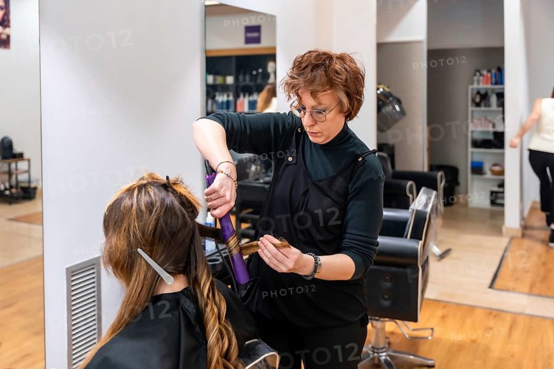 Hairdresser curling long hair with a hot tool in a modern salon, expertly creating soft waves and precise curls during a professional styling appointment for a female client