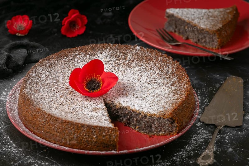 Sliced poppy seed cake on red plates with powdered sugar and poppies on a dark surface