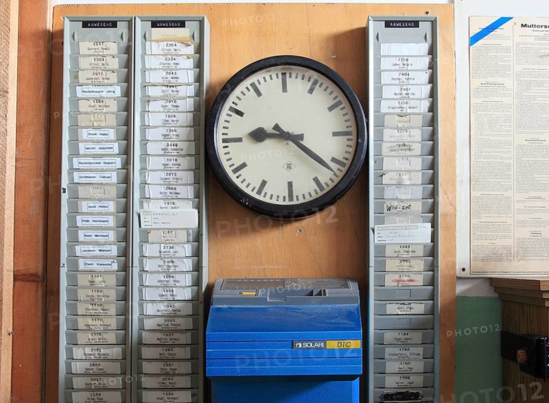 Office scene around 1972, lost place, abandoned location, historic time recording system from the 1950s, which contains a Solari DTC time clock, mechanical time clock, time clock for recording working time. The numbered stamp cards of the employees are stuck in the wall holders