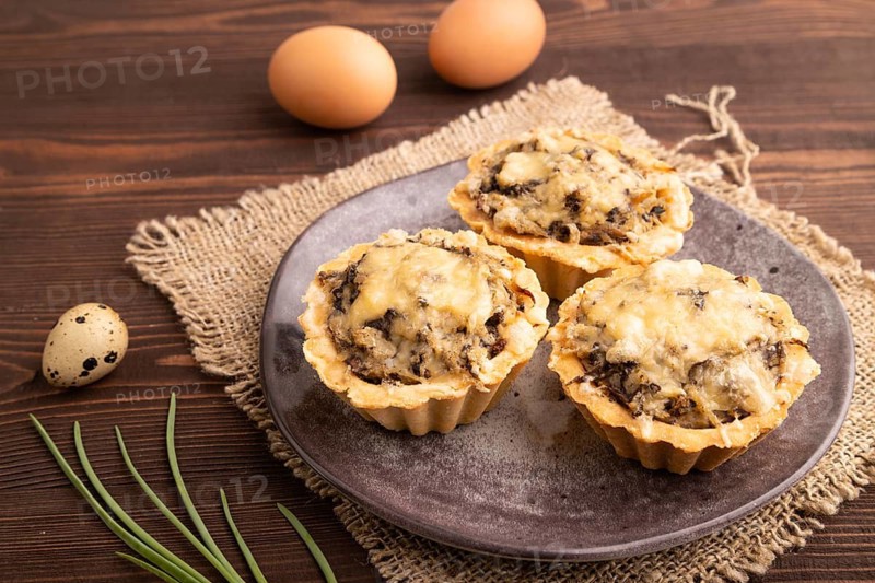 Tartlets with meat and cheese on brown wooden background and linen textile. side view, close up