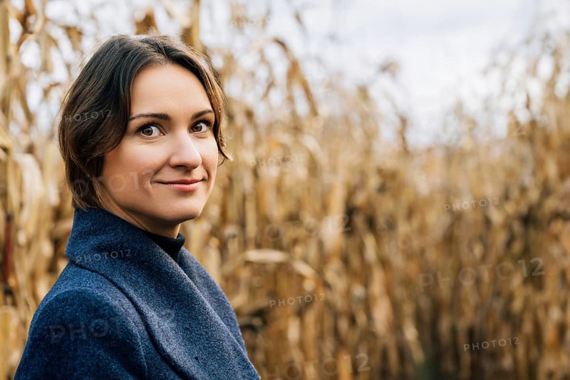 Portrait of confident smiling young short-haired woman in autumn in the middle of a cornfield