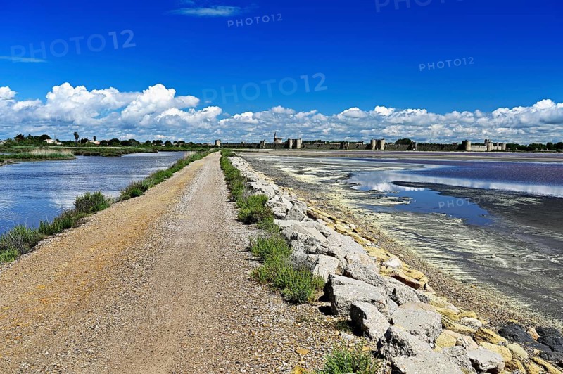 Extensive salt marshes of the Salins du Midi criss-crossed by canals and roads, the historic city wall in the back, Aigues-Mortes, Camargue, southern France, France