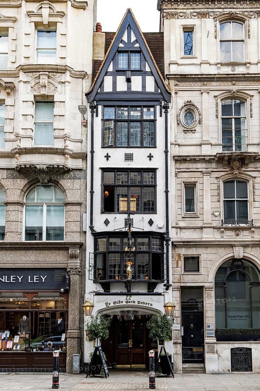 The narrow black and white timber framed frontage of Ye Olde Cock Tavern rises above Fleet Street, a historic pub with origins before the seventeenth century that was reconstructed on this site in the 1880s when its earlier premises were needed for a Bank of England branch. London, England, United Kingdom