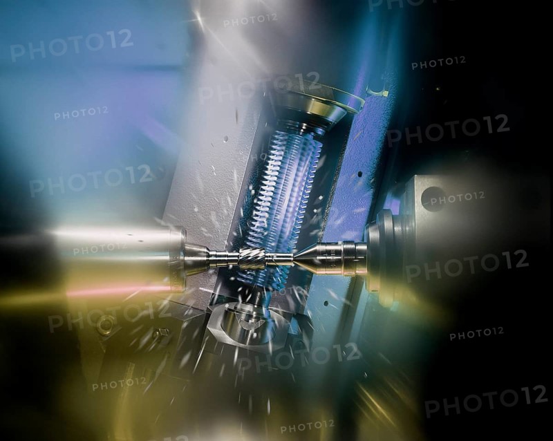 CNC controlled gear hobbing machine precisely machining a metal gear with cutting tool, flying chips and dramatic industrial lighting in modern manufacturing. Keywords: