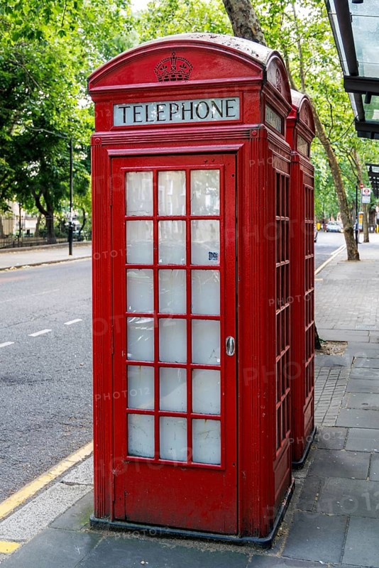 A pair of cast iron K2 telephone kiosks, designed by Sir Giles Gilbert Scott and introduced from 1926, stand on a tree lined London pavement, their domed roofs and glazed panels making the red kiosk an enduring symbol of British street furniture. London, England, United Kingdom