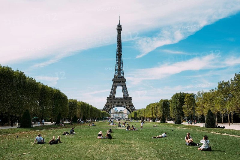 People sit and lie on the grass of the Champ de Mars and enjoy a sunny day with a direct view of the imposing Eiffel Tower. Paris, Paris Department, Ile-de-France, France