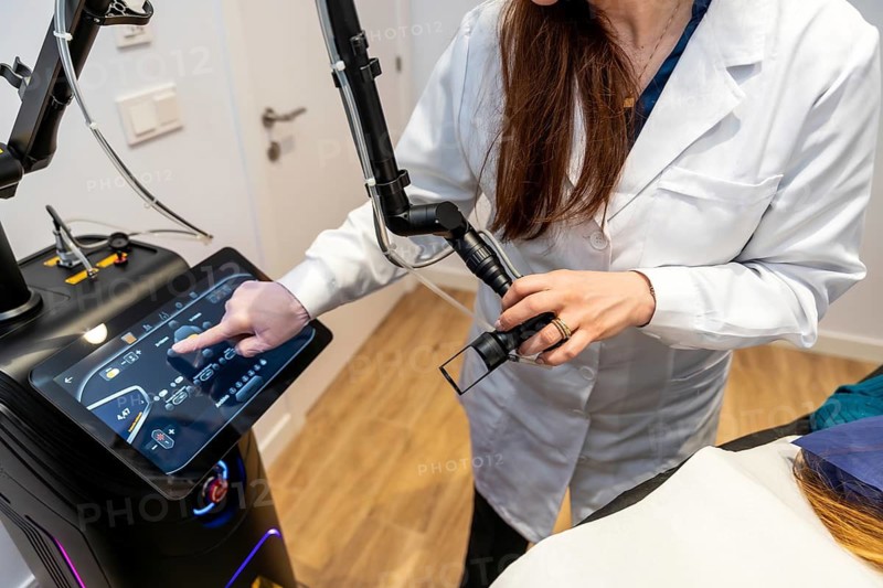 Aesthetician in a white lab coat controlling a professional laser hair removal machine with a touchscreen and preparing a treatment, focusing on beauty and skin care