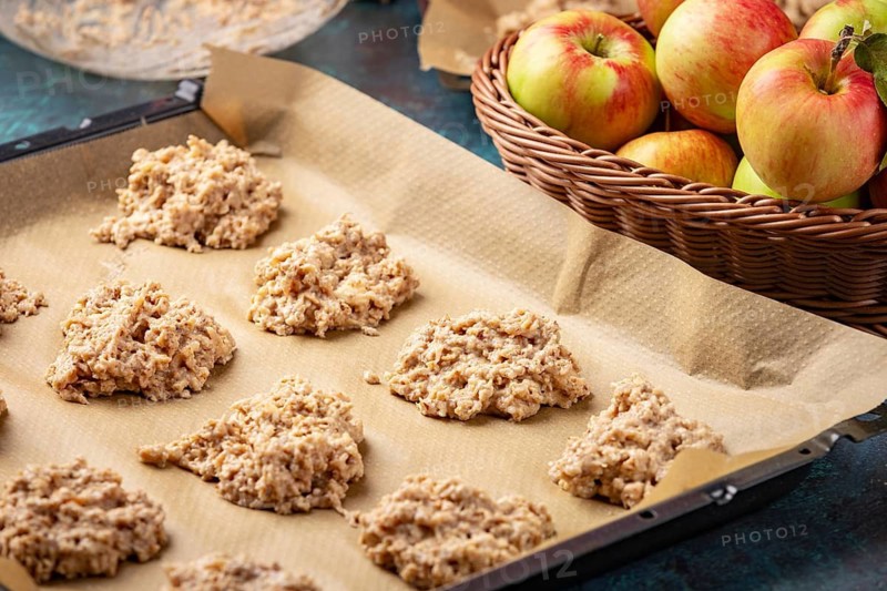 Raw cookies on a baking sheet next to apples in a basket