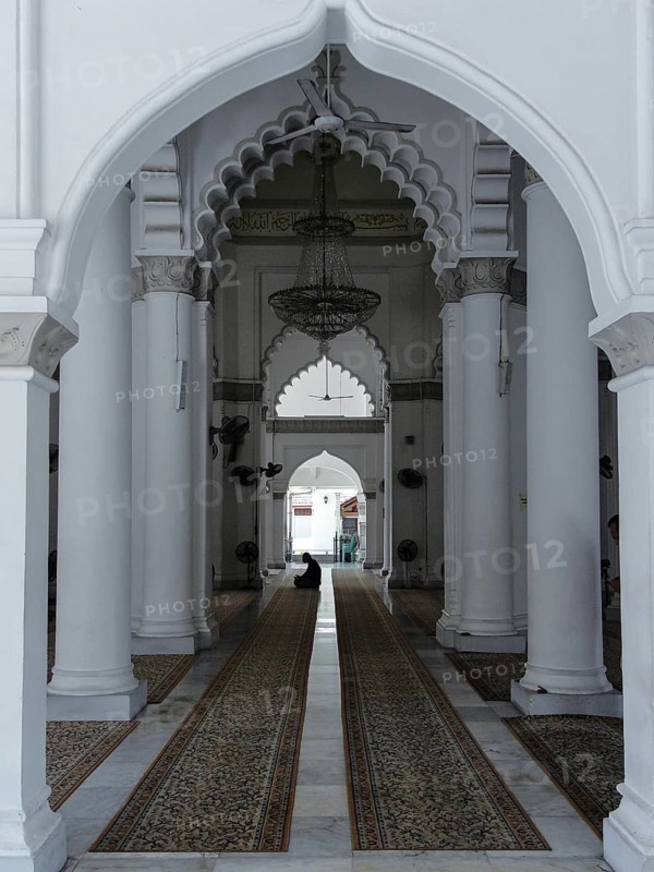Kapitan Keling Mosque, GeorgeTown Penang Malaysia, perspective, Interior of a mosque with a person praying, featuring arches, chandeliers, and carpets in a serene atmosphere, George Town, Penang, Malaysia