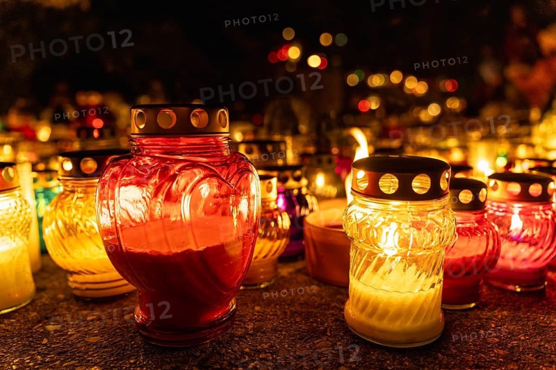 Heart-shaped candle among glowing candles in the night at cemetery on all saints day, day of the dead, or memorial day. A huge number of multicolored burning candles and lamps at a cemetery during All Saints' Day celebrations. Warsaw, Poland