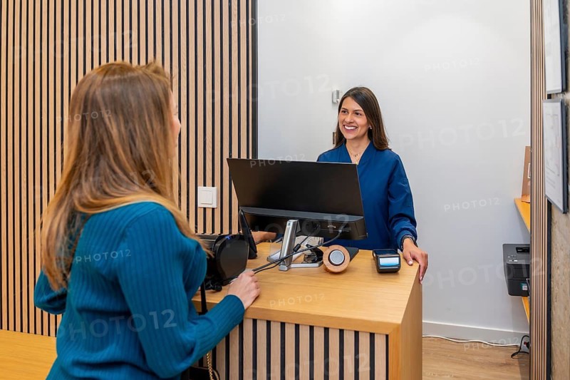 Client interacting with a smiling woman working as a receptionist at a modern aesthetic clinic or laser hair removal center, providing customer service and managing appointments