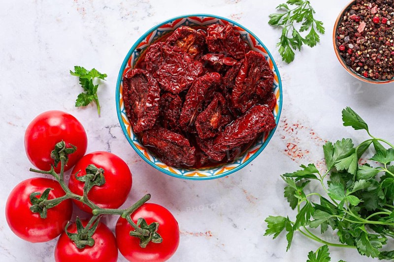 Dried tomatoes, in a ceramic bowl, with fresh herbs and spices, on a white marble surface, top view, no people