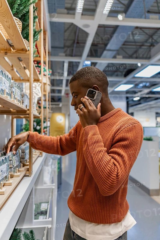 Man is standing in store looking at home decor items on shelves. He is holding a phone while reaching for a product