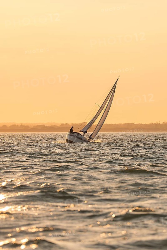 A sailboat at a gentle sunset, golden sky and calm sea, Howth, Ireland