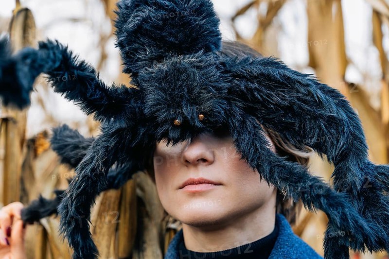 A huge black shaggy toy spider on a woman's head closes her eyes. Halloween Party Costumes and Decorations