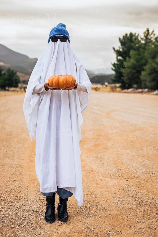 Funny Halloween ghost holding pumpkin outdoors. Viral seasonal content, creative costume idea and modern autumn lifestyle concept.