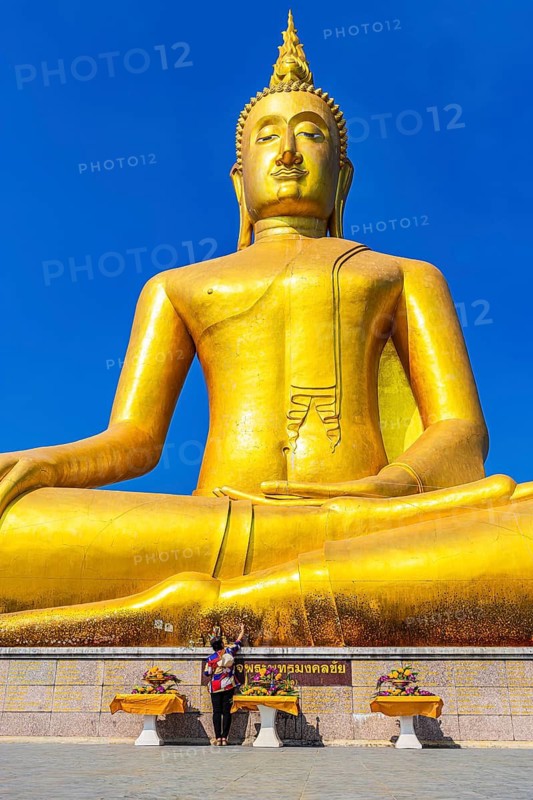 Monumental golden Buddha statue against deep blue sky, visitor and offerings at the pedestal, Bangkok, Thailand