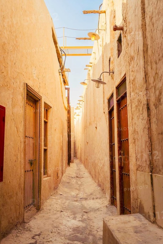 Doha Qatar Katara Cultural Village narrow traditional alley mud brick walls heritage architecture sun flare travel tourism Middle East Qatari culture exploration sunny