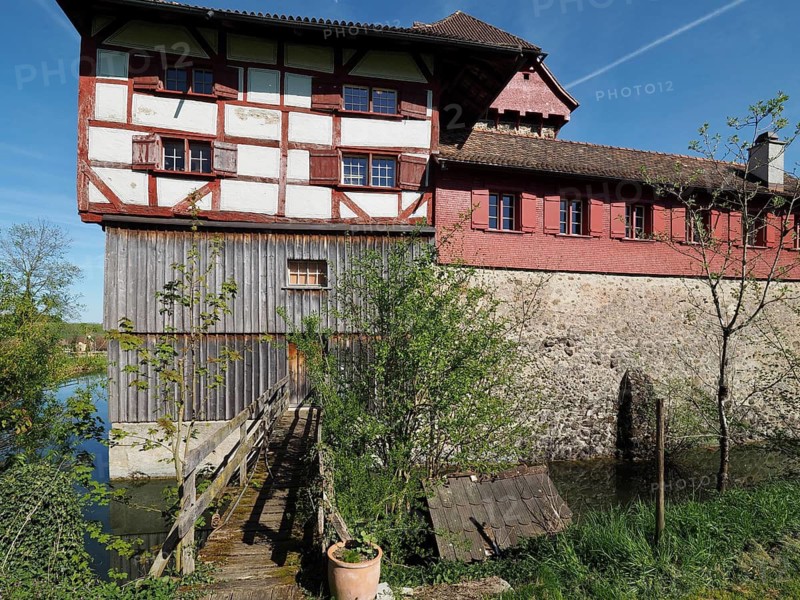 Medieval castle with half-timbered structure with red and white structure, small wooden bridge and green surroundings under blue sky, Hagenwil, Amriswil, Canton of Thurgau, Lake Constance region, Switzerland
