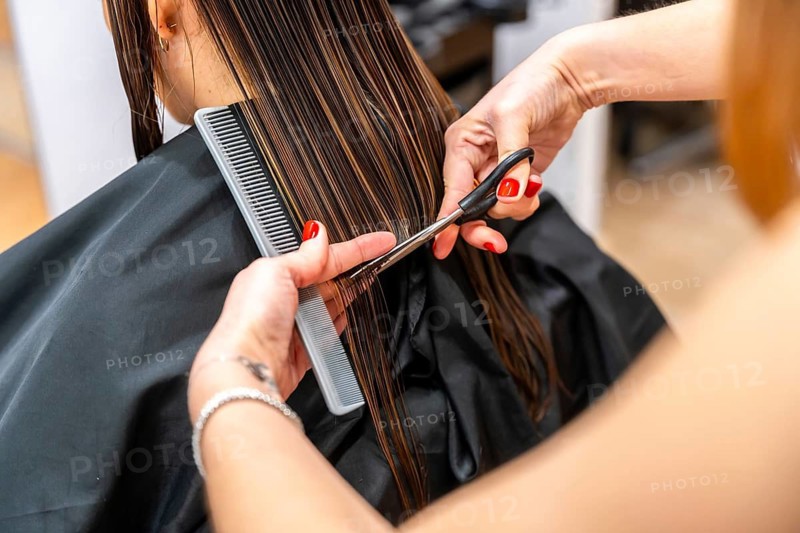 Professional hairdresser's hands with red nails expertly trimming the wet, brown hair of a female client during a haircut session at a beauty salon, focusing on hair care and contemporary styling