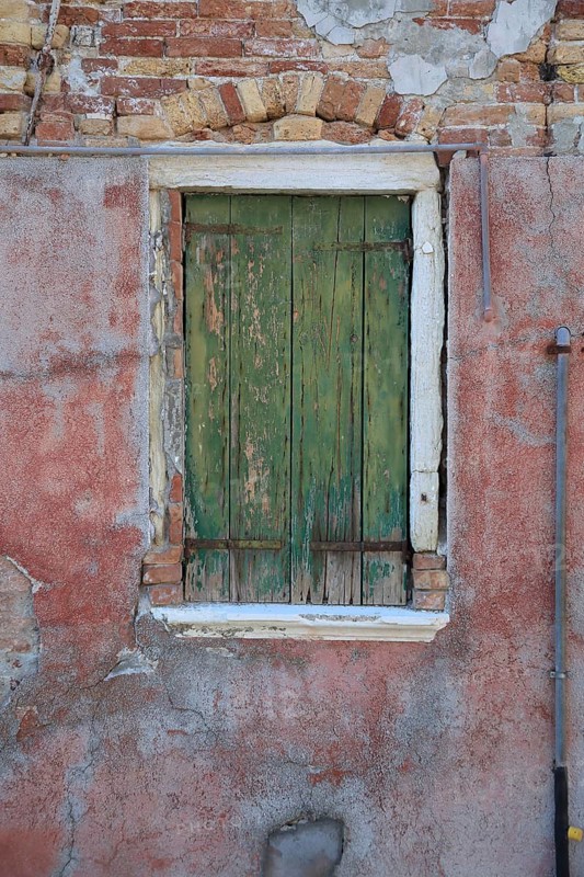 Old window with green wooden shutters in front of a heavily weathered red wall, windows with green shutters, colorful houses on the island of Burano, Venice, Veneto, Italy