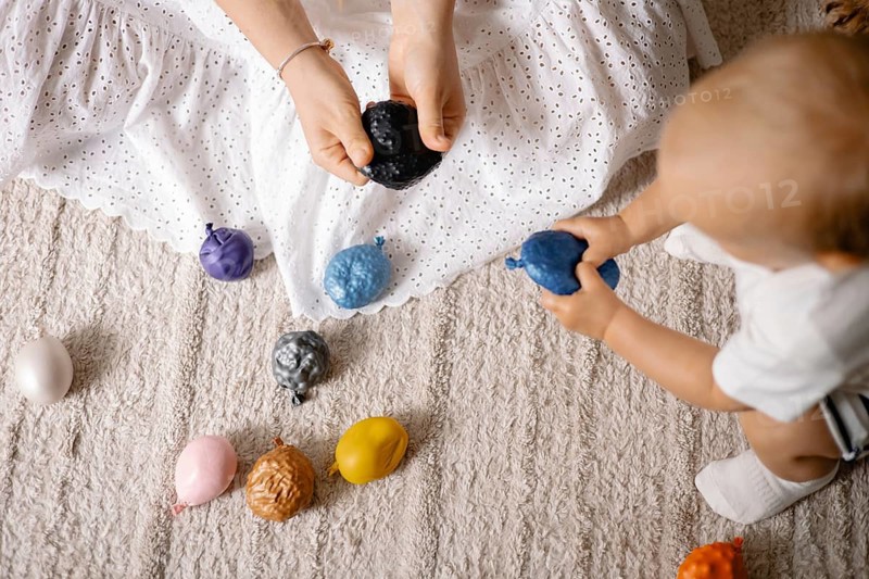 A toddler plays with colorful toys while interacting with a mother, signifying active playtime on the floor