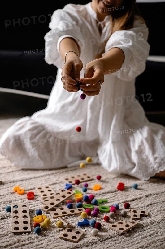 Person dropping colorful balls with scattered wooden toys on the floor