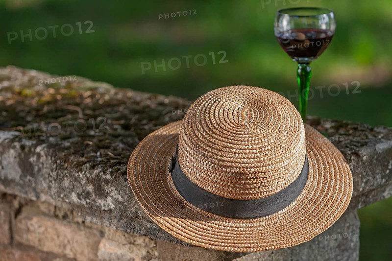 Straw hat lying on a wall with a glass of red wine in the background, Provence, France