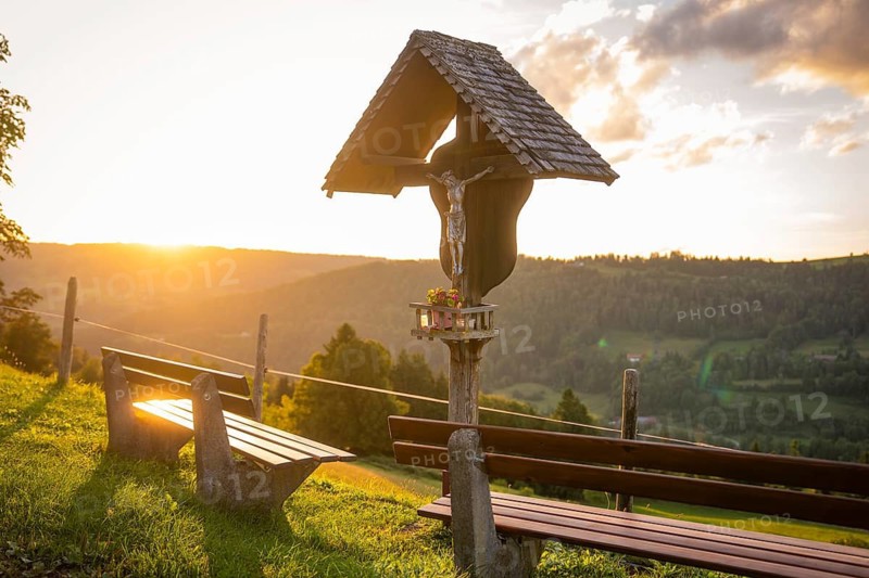 A wooden cross near benches with a view of a beautiful landscape at sunset, Oberstaufen region, Allgäu, Bavaria, Germany