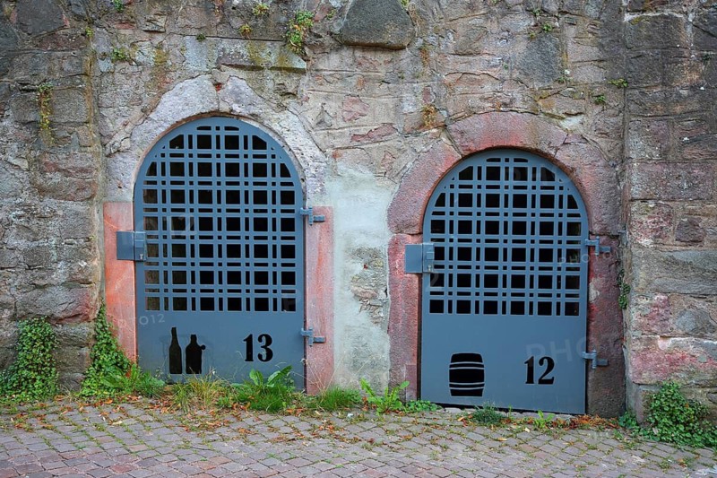 Two doors with bars to the wine cellar, cellar doors with metal mesh and house numbers, wine culture symbols, wine bottles, wine barrel, numbers 12, 13, metal doors, stone wall, Mittweida, Saxony, Germany