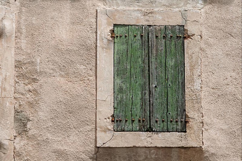 Weathered green wooden shutters in front of an old, rough wall, Provence, France
