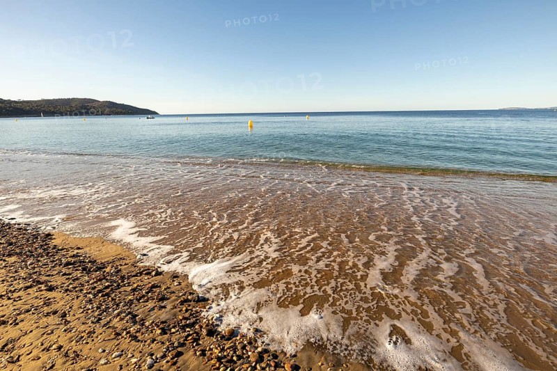 Low beach-level viewpoint over wet sand and sea foam with calm blue water, yellow buoys, distant coastline, and clear summer sky on Gigaro Beach, La Croix-Valmer, Gigaro Beach, Var, Provence-Alpes-Cote d'Azur, France