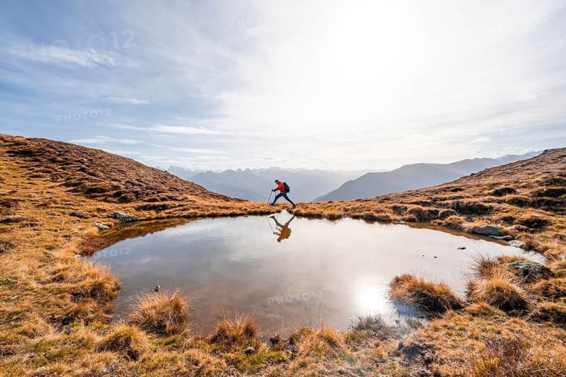 Mountaineer hiking with poles, reflected in a small mountain lake on the Krahberg, mountain panorama in autumn, Venet crossing, Ötztal Alps, Tyrol, Austria