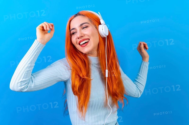 Redhead woman in studio photography smiling dancing on a blue background