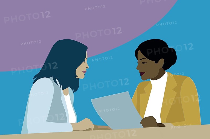 Two women engage in a business discussion, reviewing a document together at a table, with a vibrant backdrop adding a modern touch to the setting