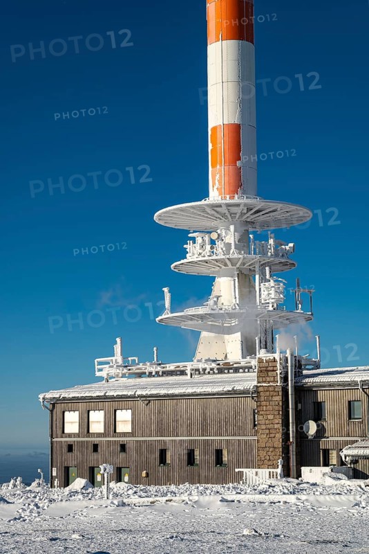 Telecommunication tower and technical building covered in snow and ice on the Brocken summit, on a sunny winter day under clear blue sky, Harz National Park, Saxony-Anhalt, Germany