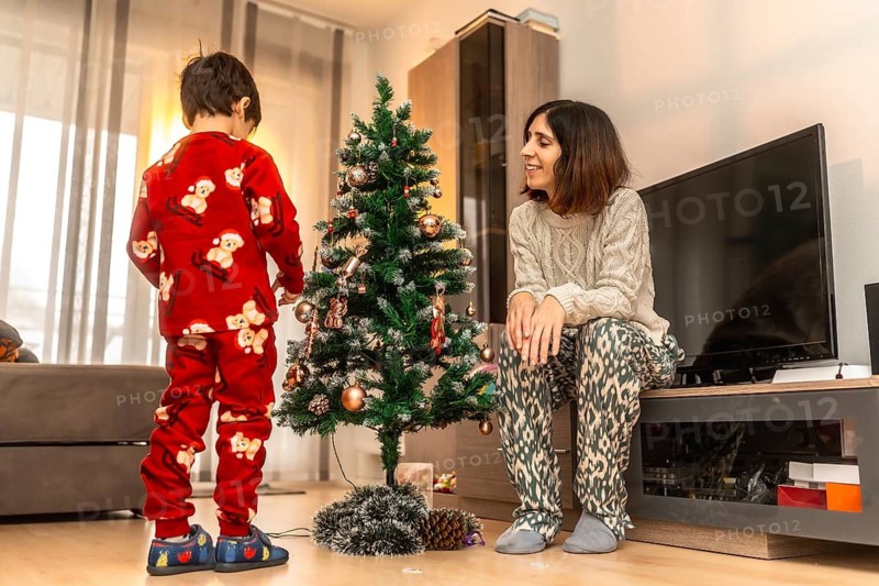 Mother and son sharing a special holiday moment together in the living room, decorating a christmas tree with ornaments while wearing comfortable pajamas