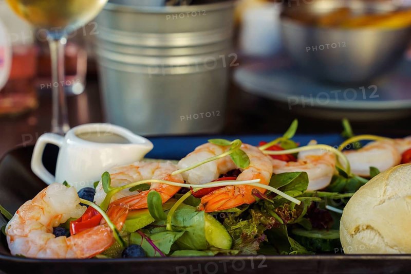 Shrimp salad on a table in a restaurant close-up. Healthy food, Fresh shrimp salad with greens and tomatoes, served with dressing and bread on a dining table
